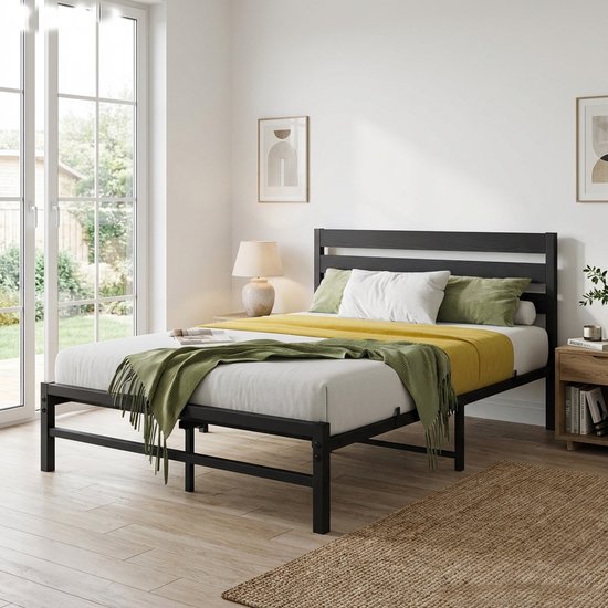 Modern zwart metalen bedframe met houten hoofdbord, opgemaakt met wit beddengoed, groen en geel plaid.