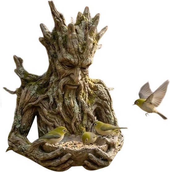 Bodemloze boomman sculptuur met mos, houdt een voederbak vast, met vogels.