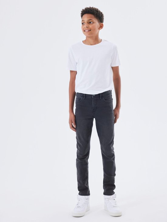 Jongen met witte t-shirt en grijze slim fit spijkerbroek, staand.