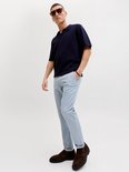 Man met zonnebril, donkerblauw poloshirt en lichtblauwe pantalon met ruitpatroon en omgeslagen pijpen.