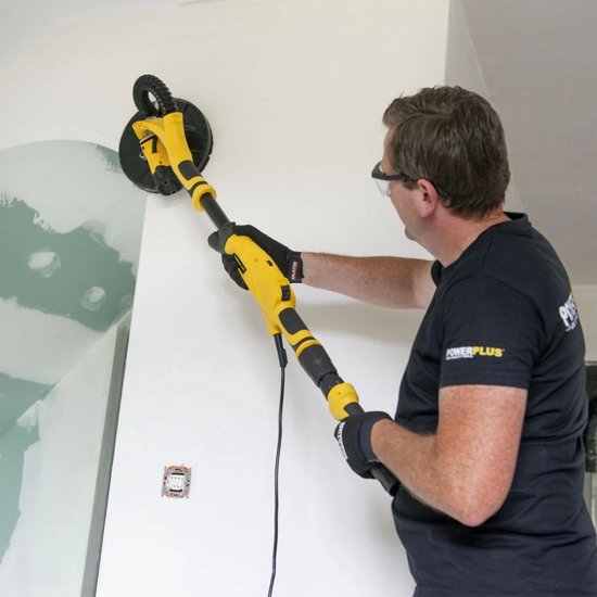 Man met veiligheidsbril schuurt een muur met een gele en zwarte telescoopschuurmachine.