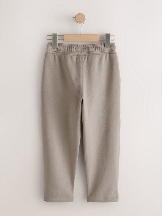 Grijze joggingbroek aan een kledinghanger, met elastische tailleband en trekkoord.