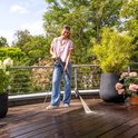 Vrouw reinigt houten terras met Karcher hogedrukreiniger, met planten en hek op balkon.