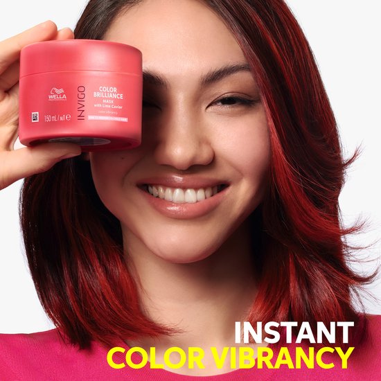 Vrolijke vrouw met rood gekleurd haar houdt een pot Wella Invigo Color Brilliance masker voor haar gezicht. Tekst: 'Instant Color Vibrancy'.