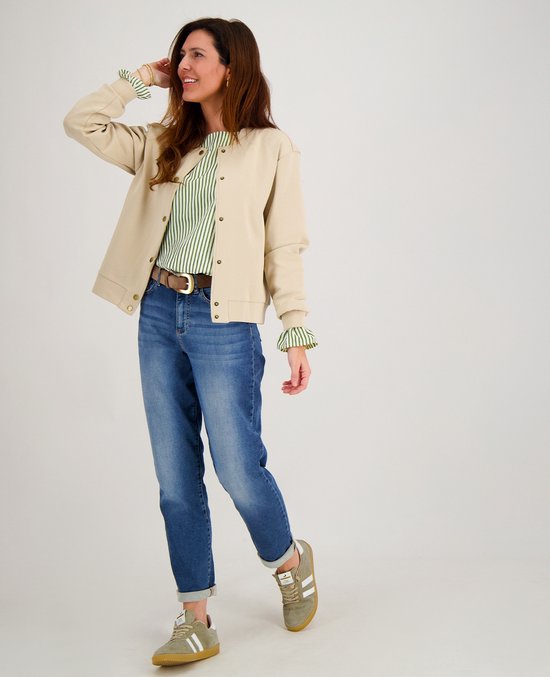 Vrouw met een beige bomberjack, een groen gestreept shirt, spijkerbroek en groene sneakers.