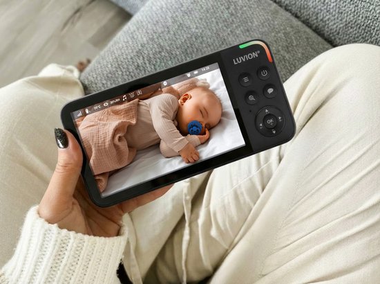 Een babyfoon met scherm toont een slapende baby met een blauwe fopspeen, aangekleed in een beige romper.