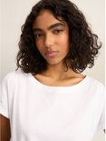 Een vrouw met krullend donker haar draagt een wit T-shirt met opgerolde korte mouwen en een ronde hals.