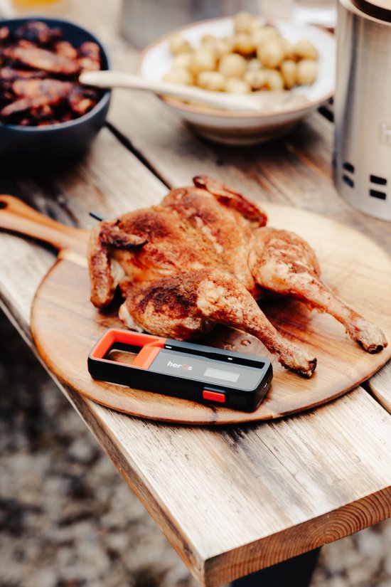 Gegrilde kip op een houten plank met een zwarte en rode herQs thermometer ernaast.