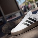 Gedetailleerde opname van witte Adidas VL Court 3.0 sneakers met bruine zolen en zwarte strepen.