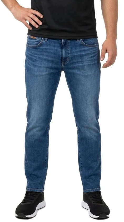Model draagt een blauwe Wrangler slim fit spijkerbroek met een zwart t-shirt en zwarte sneakers.