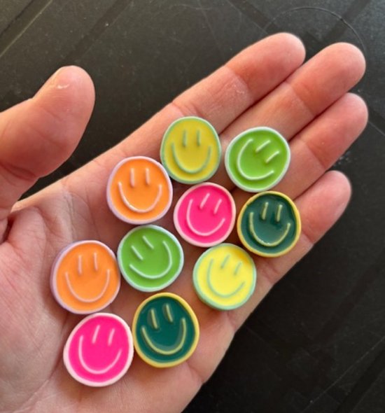 Hand vol ronde smiley magneten in pastelkleuren: roze, oranje, geel, groen en groenblauw.