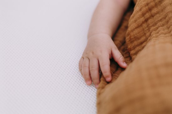 Babyhandje rustend op een witte, zacht-gestructureerde matras.