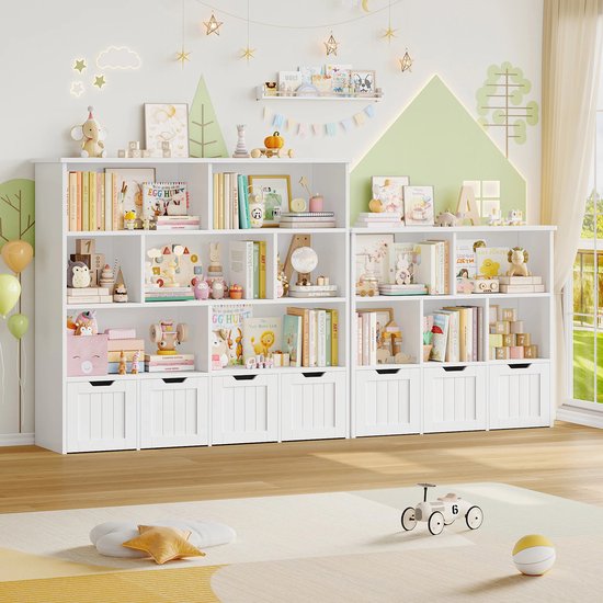 Twee witte kinderboekenkasten op een houten vloer met speelgoed en boeken, op de muur zijn bomen en sterren te zien.