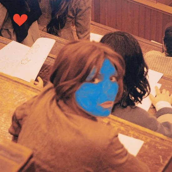 Gedetailleerde foto van een persoon met een blauw gezicht en rode lippen, kijkend over de schouder in een klaslokaal.