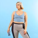 Model in blauwe crop top en grijze/zwarte sportlegging, met flesje Rit DyeMore Smoky Blue in hand.
