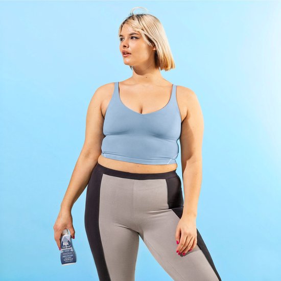 Model in blauwe crop top en grijze/zwarte sportlegging, met flesje Rit DyeMore Smoky Blue in hand.