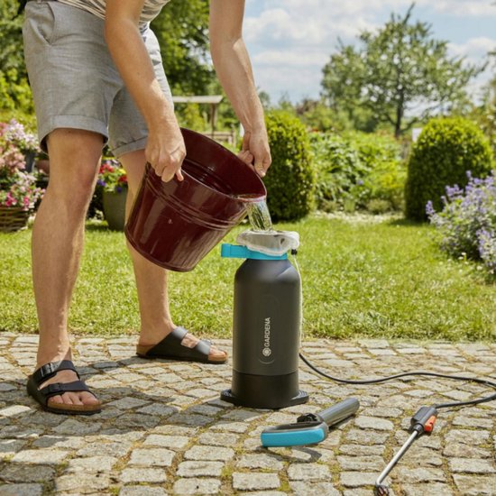Man vult donkergrijze drukspuit met blauw handvat en rode deksel met water uit een bak.