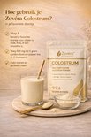 Een glas met een romige drank, een lepel en een kom met poeder naast een zak "Zuvéra Colostrum". Instructies voor gebruik.