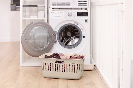 Crème wasmand gevuld met kleding, naast een open wasmachine.