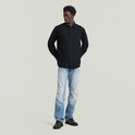 Man, hele lichaam, kijkt weg, draagt een donkerblauw regular fit overhemd, handen achter de rug.