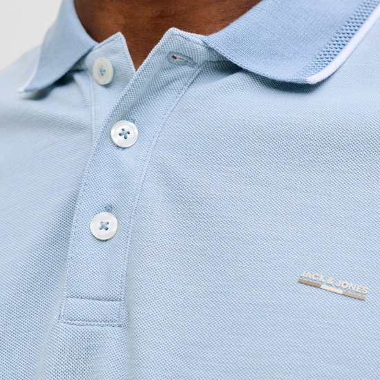 Close-up van de kraag en knopen van een lichtblauw poloshirt met logo.