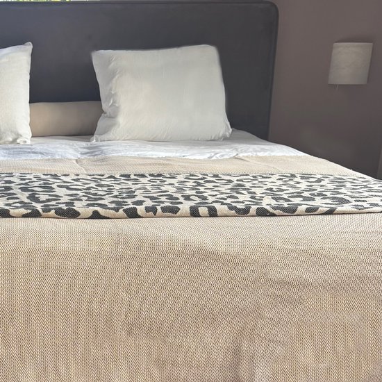 Bed met wit beddengoed en een beige sprei met zwarte panterprint.