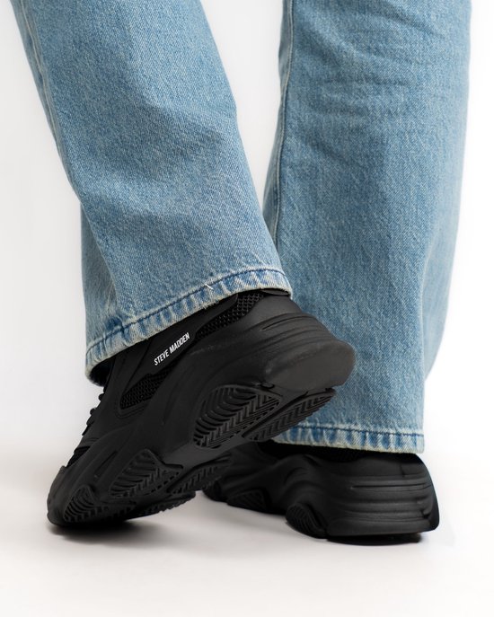 Dames met blauwe jeans dragen zwarte Steve Madden sneakers.