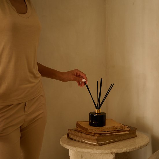 Een vrouw met beige kleding die een zwart diffuser van Ted Sparks met zwarte stokjes verplaatst.