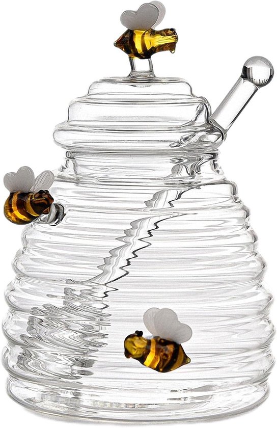 Glazen honingpot in bijenkorfvorm met decoratieve bijen en honinglepel, leeg.