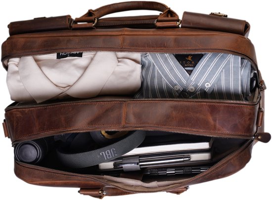 Open bruine XL leren laptoptas met opgevouwen kleding, een waterfles, koptelefoon en schriften.