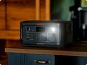 Donkergrijs Jackery Explorer 500 powerstation met oranje accenten, op een houten meubel, met de verlichting aan.