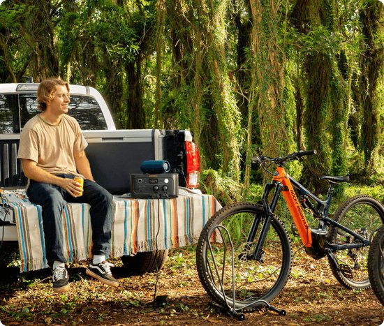 Donkergrijs Jackery Explorer 500 powerstation met oranje accenten, op de laadbak van een pick-up truck, naast een mountainbike.