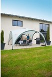 Een Coleman partytent met tafel en stoelen, naast een huis met een barbecue.