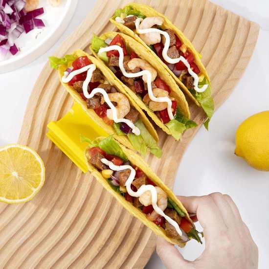 Een gele tacohouder met vier gevulde taco's, en een hand die een taco oppakt.