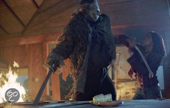 Jason Voorhees met een harige jas en masker, staat tegenover een vrouw die een koevoet omhoog houdt in een brandende kamer.