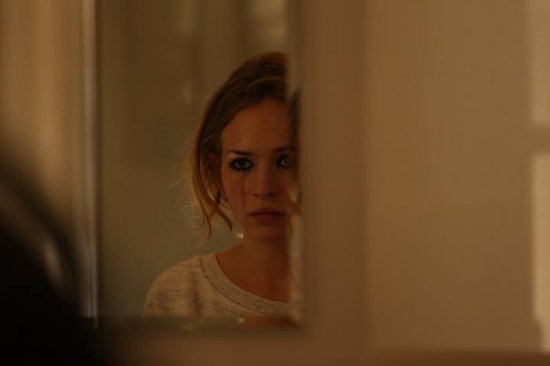 Jonge vrouw met make-up op haar ogen kijkt in de spiegel, lichte trui.