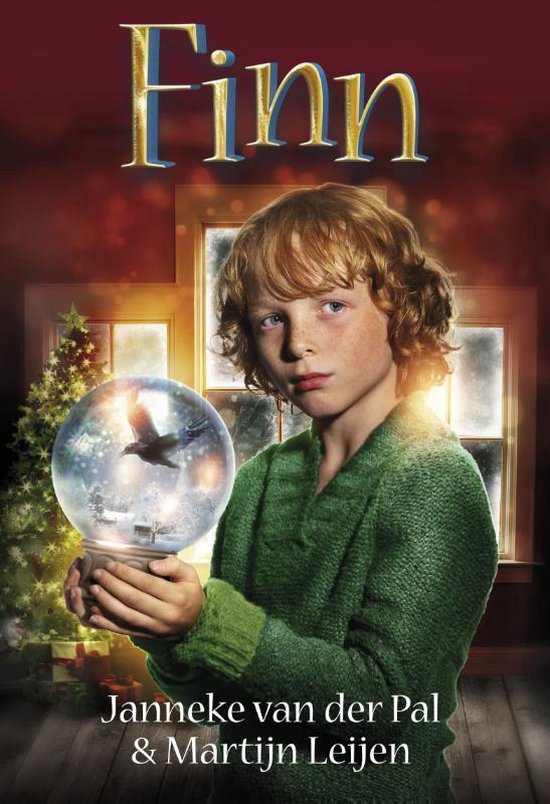 Een jongen met rood haar, Finn, met een groene trui, houdt een sneeuwbol met een raaf vast voor een kerstboom.