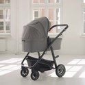 Grijze kinderwagen met reiswieg, zwarte duwstang en wielen, in lichte kamer.