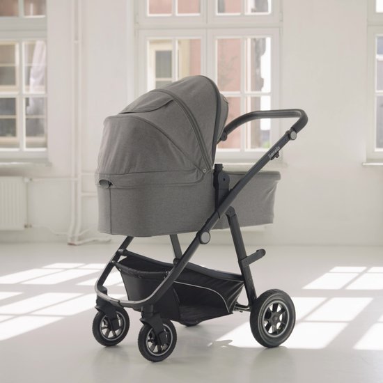 Grijze kinderwagen met reiswieg, zwarte duwstang en wielen, in lichte kamer.