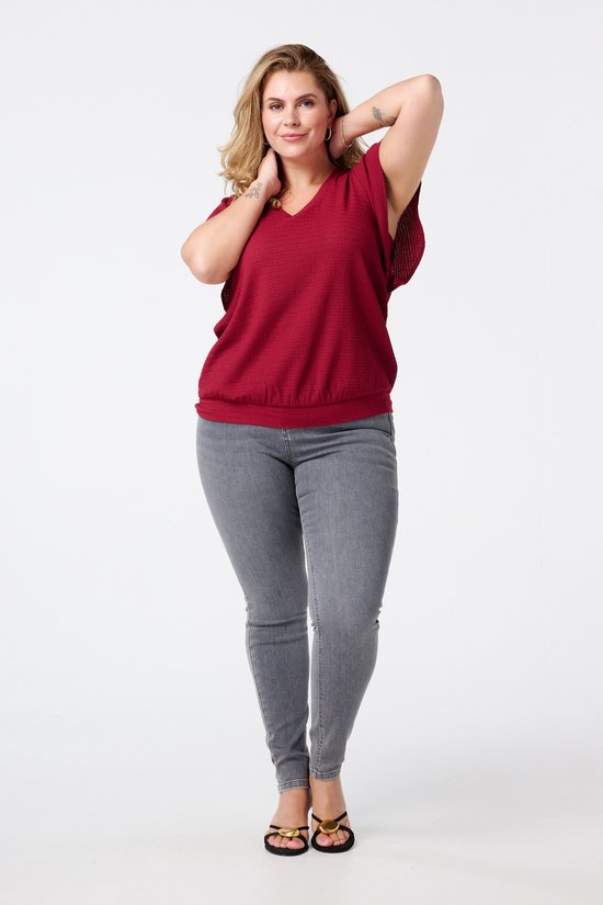 Vrouw in grijze skinny jeans met hoge taille en wijnrode top.