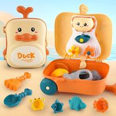 Open oranje speelgoedkoffer met eend-thema op strand, met zandschepjes en diverse bad- en zandspeeltjes.