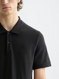 Detail van een zwarte poloshirt met korte mouwen en een geborduurd logo.