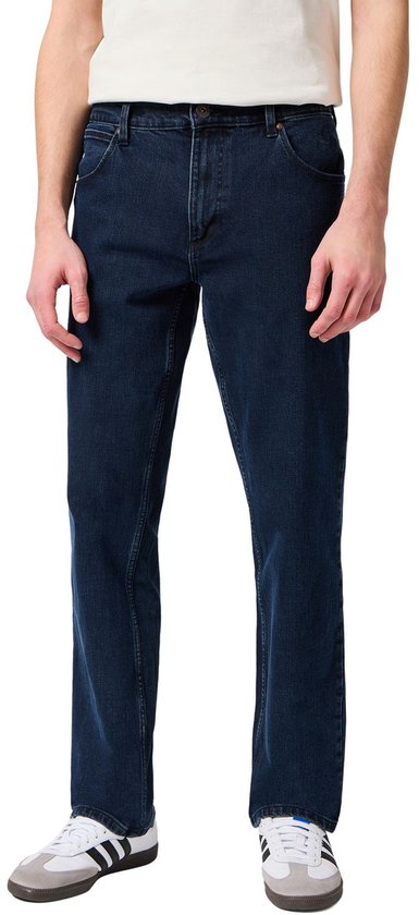 Man in een donkerblauwe spijkerbroek, staand, voorkant.