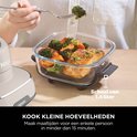 Kleine glazen schaal met zalm en broccoli, met een persoon die broccoli prikt.