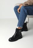 Mannequin portant des bottines noires à imprimé crocodile, fermeture éclair et boucle argentée.