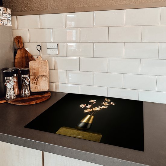 Zwarte inductiebeschermer met boeket bloemen op een gouden voetstuk, op een donker aanrecht.