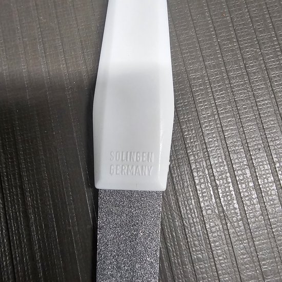 Detail van de witte handgreep van een nagelvijl met 'SOLINGEN GERMANY' erop.