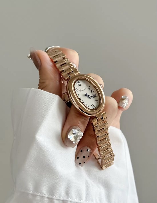 Hand met lange, versierde nagels die een rosé gouden dameshorloge vasthoudt.