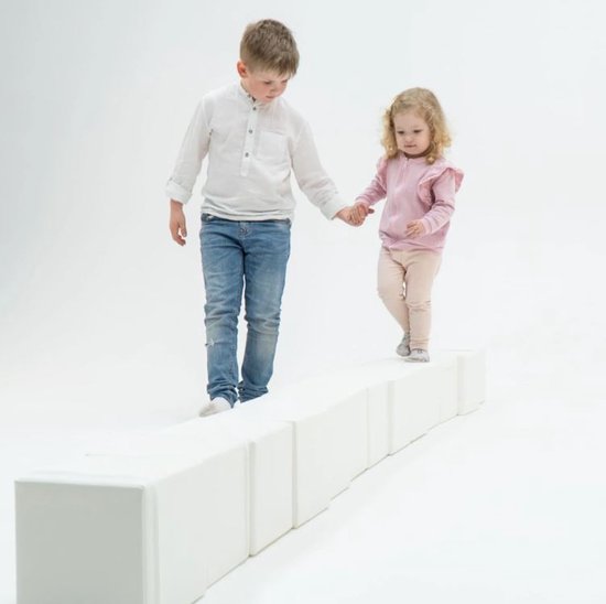 Twee kinderen lopen hand in hand over een rij van witte foam bouwblokken.