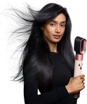 Vrouw met lang, donker, wapperend haar houdt een beige en rosé-gouden Dyson föhn vast.